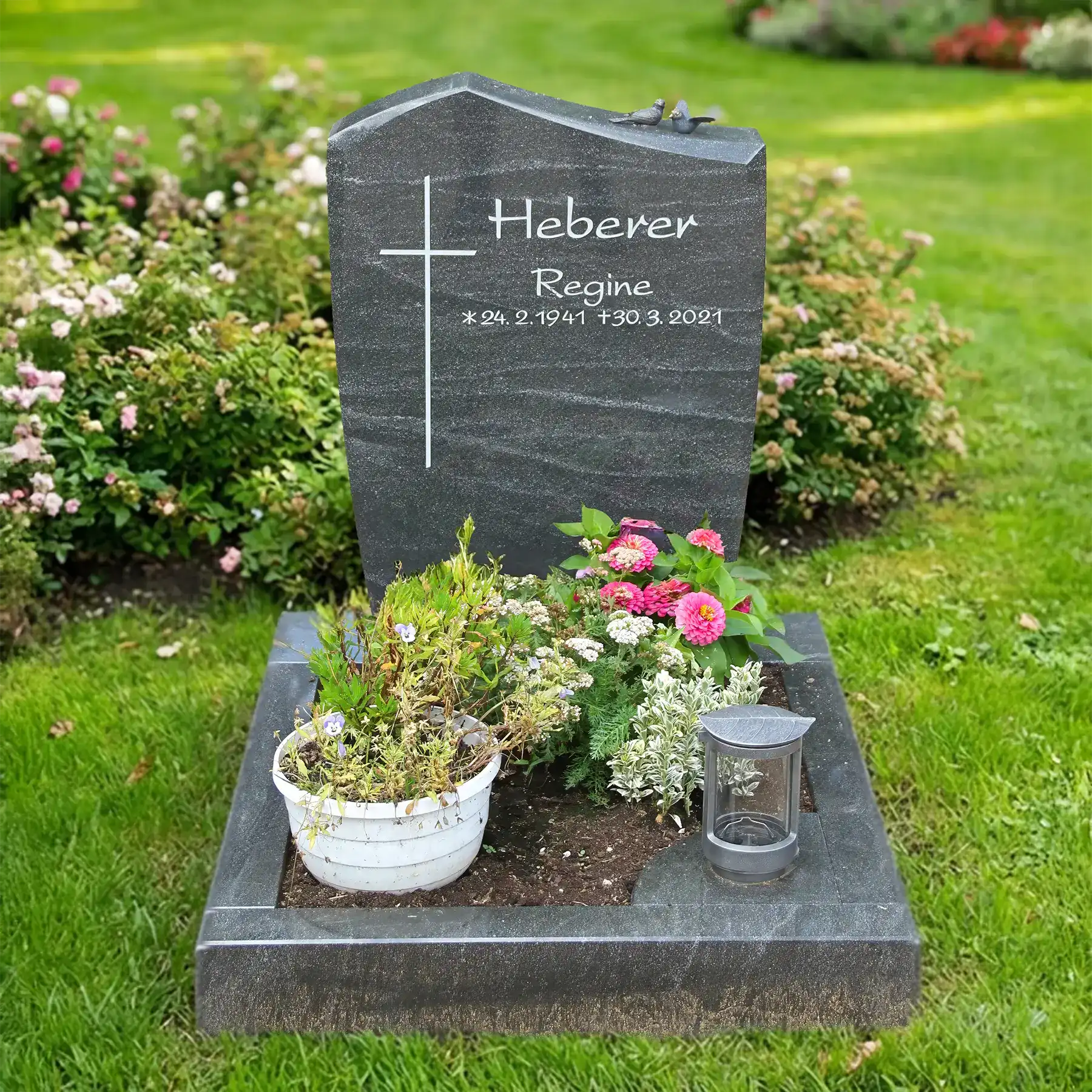 Urnengrabstein aus grünem Alexandria Granit, poliert mit einfachem Kreuz, umgeben von Blumen und Dekorationen, ideal für eine würdevolle Grabgestaltung.