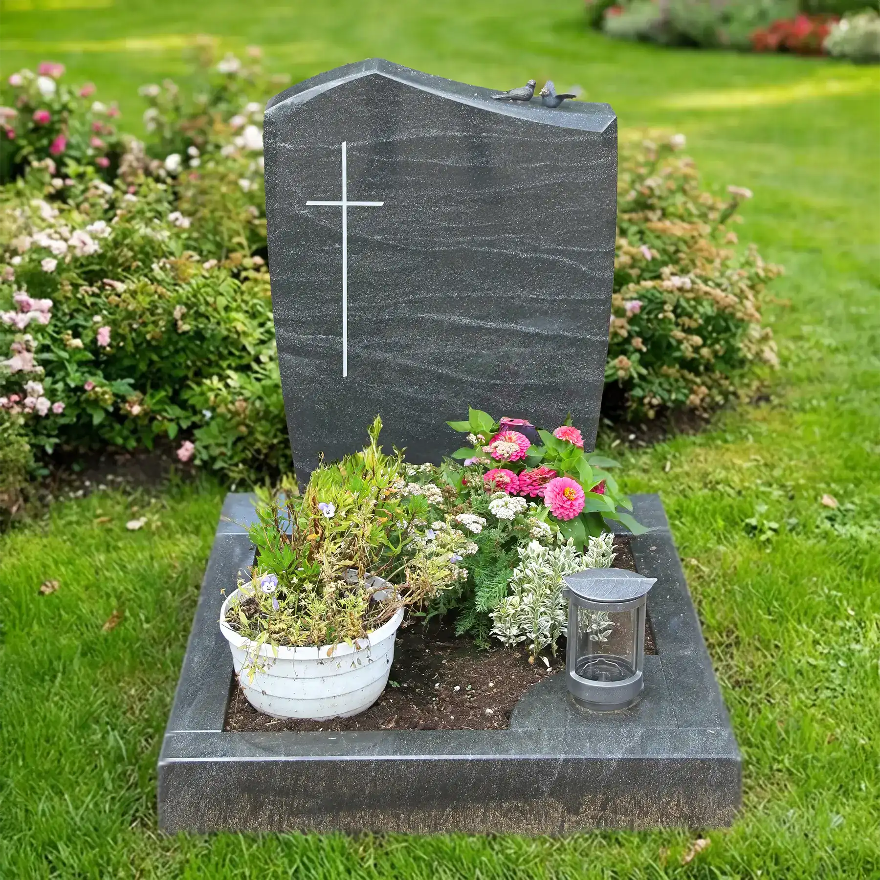 Grabstein aus grünem Alexandria Granit mit Kreuz, gepflegte Grabstätte mit Blumen und Laterne.